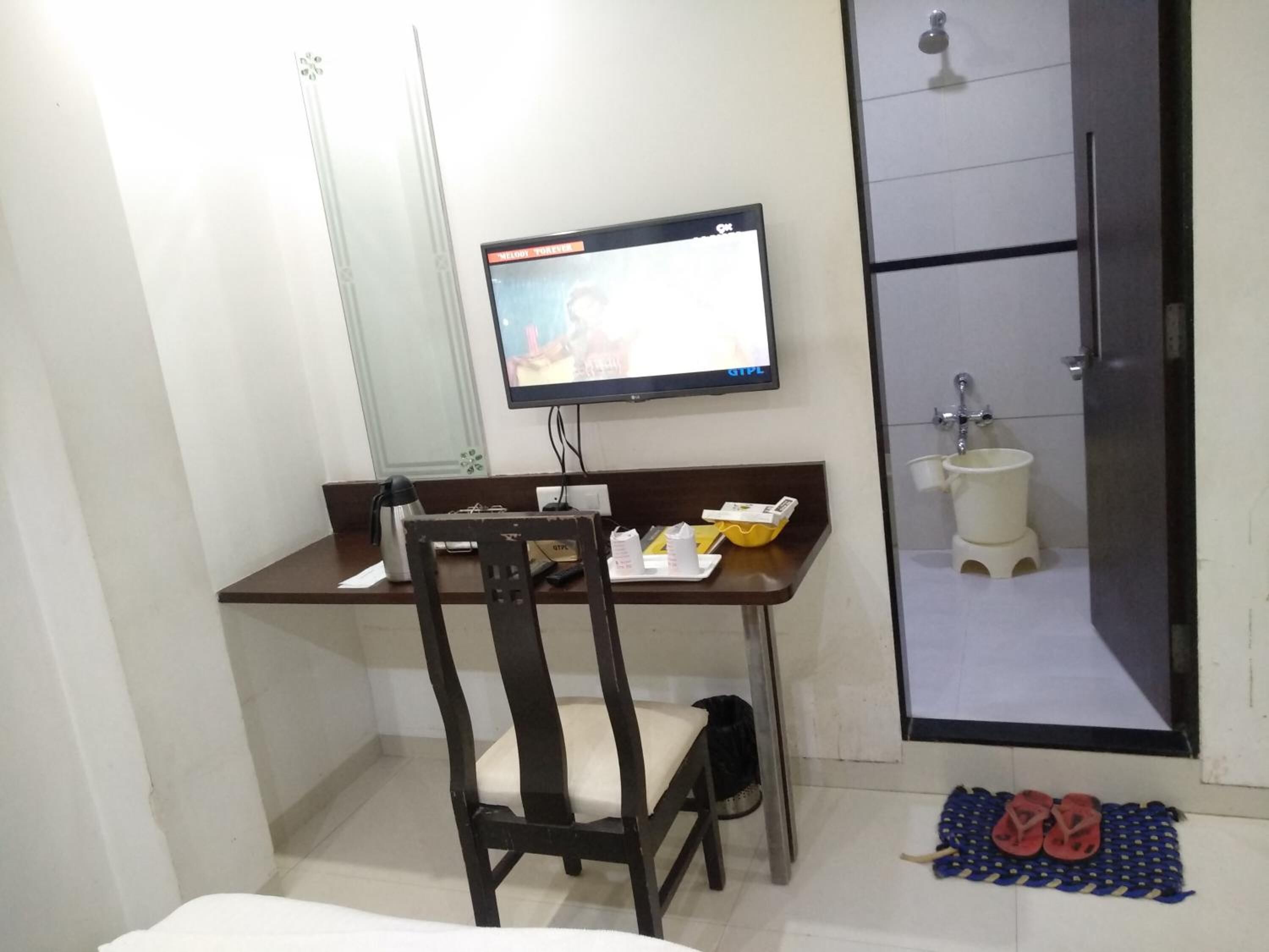 Quarto de hotel com escrivaninha, cadeira, televisão e banheiro pequeno com vaso sanitário e pia.