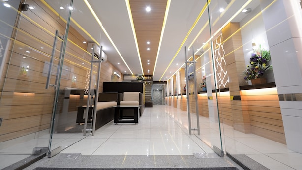 En moderne hotellobby med glasafskærmninger, en reception, et loungeområde og dekorative planter.