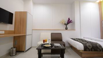 A modern hotel room with a bed, a TV, a small table with a newspaper, and a vase with flowers.