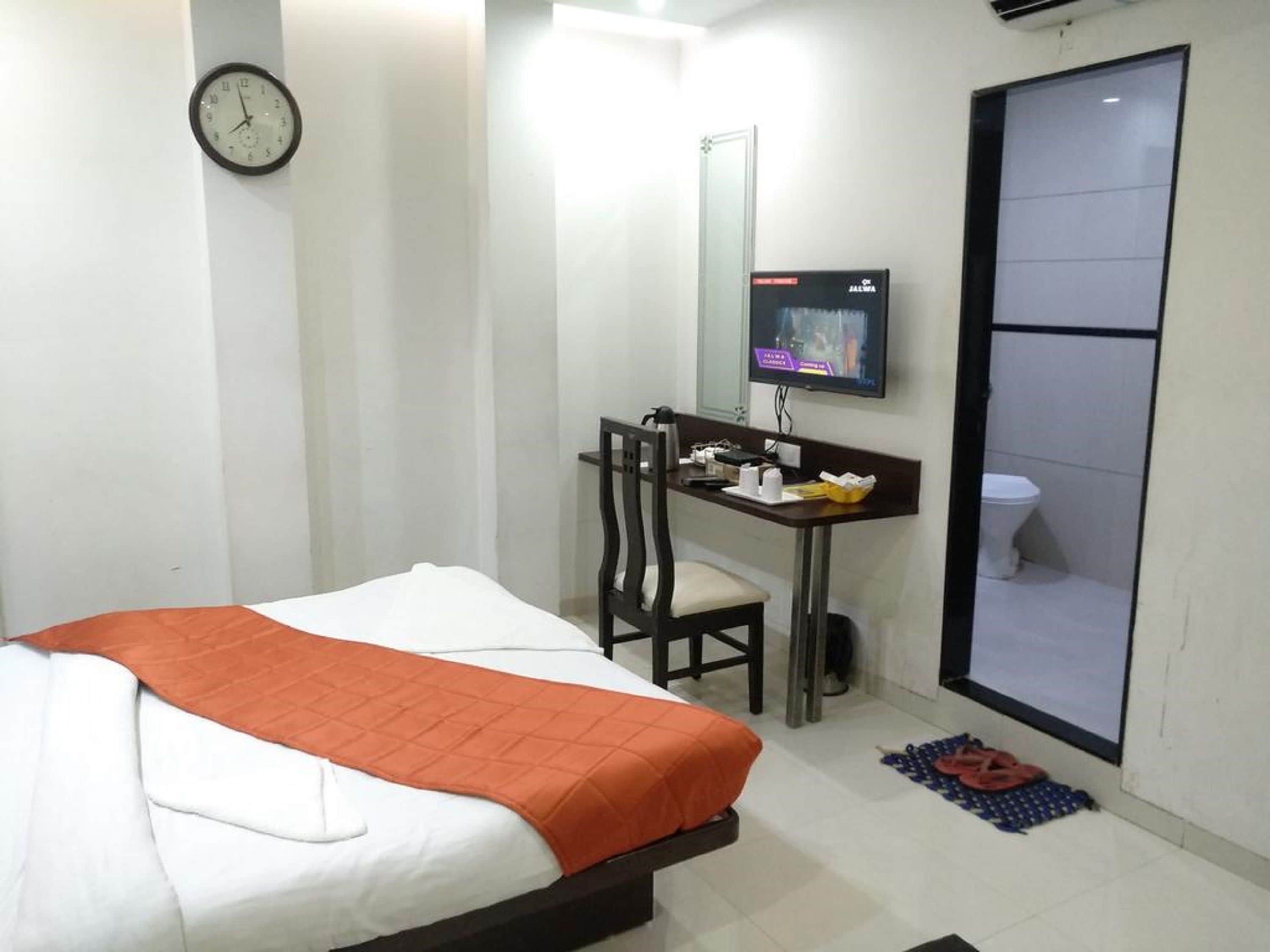 A hotel room with a bed, a desk with a chair, a television, and a bathroom.