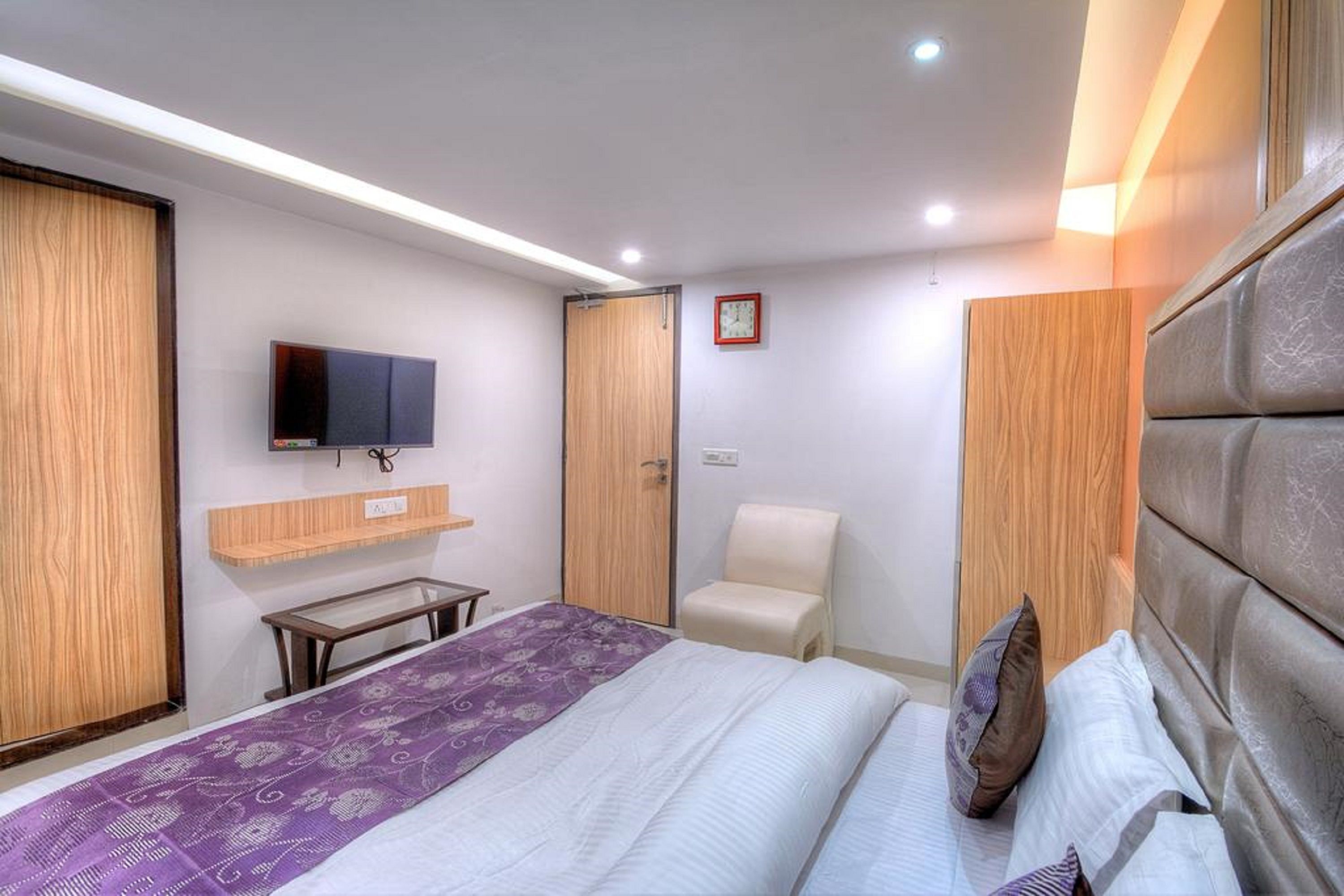 Quarto de hotel moderno com uma cama grande, televisão de tela plana na parede, guarda-roupa de madeira, uma mesinha e uma cadeira.