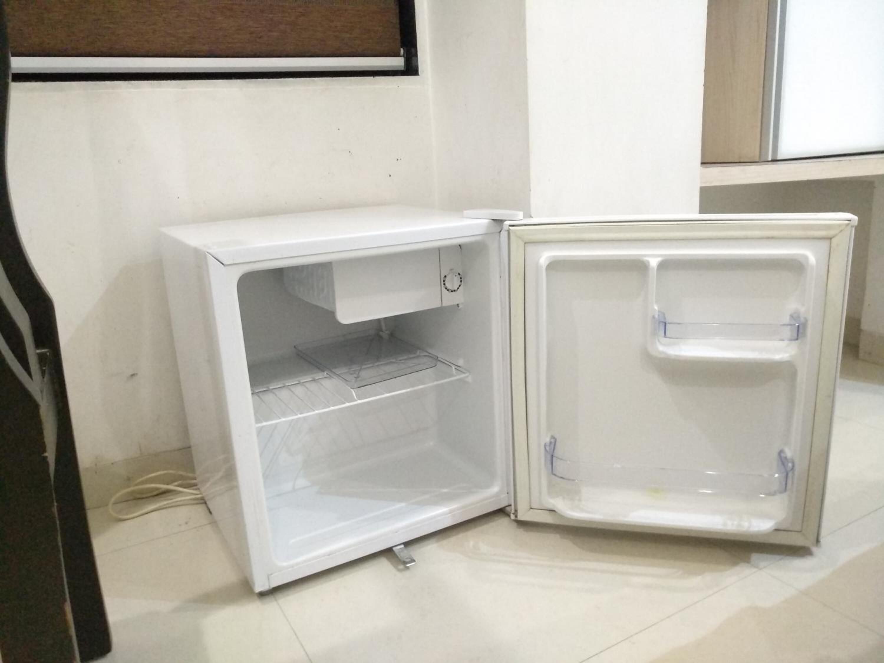 A compact white refrigerator with a single door and a small shelf, placed in a corner of a room with tiled flooring.