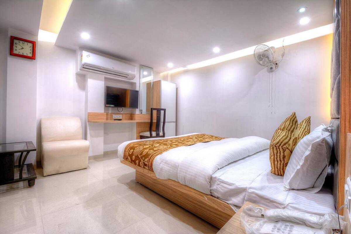 A modern hotel room with a bed, a desk, a chair, and an air conditioning unit.