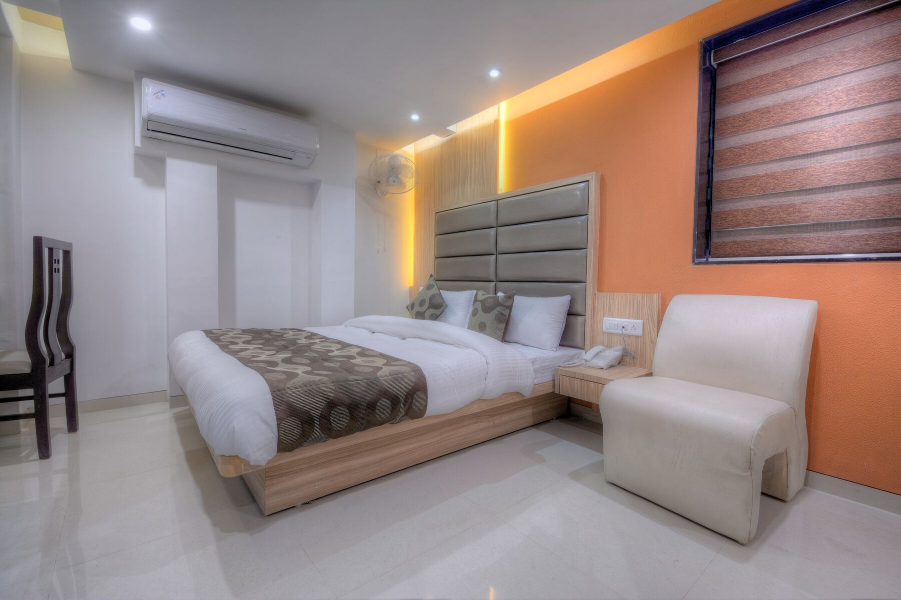 Een moderne slaapkamer met een bed, nachtkastje, stoel en een airconditioning.