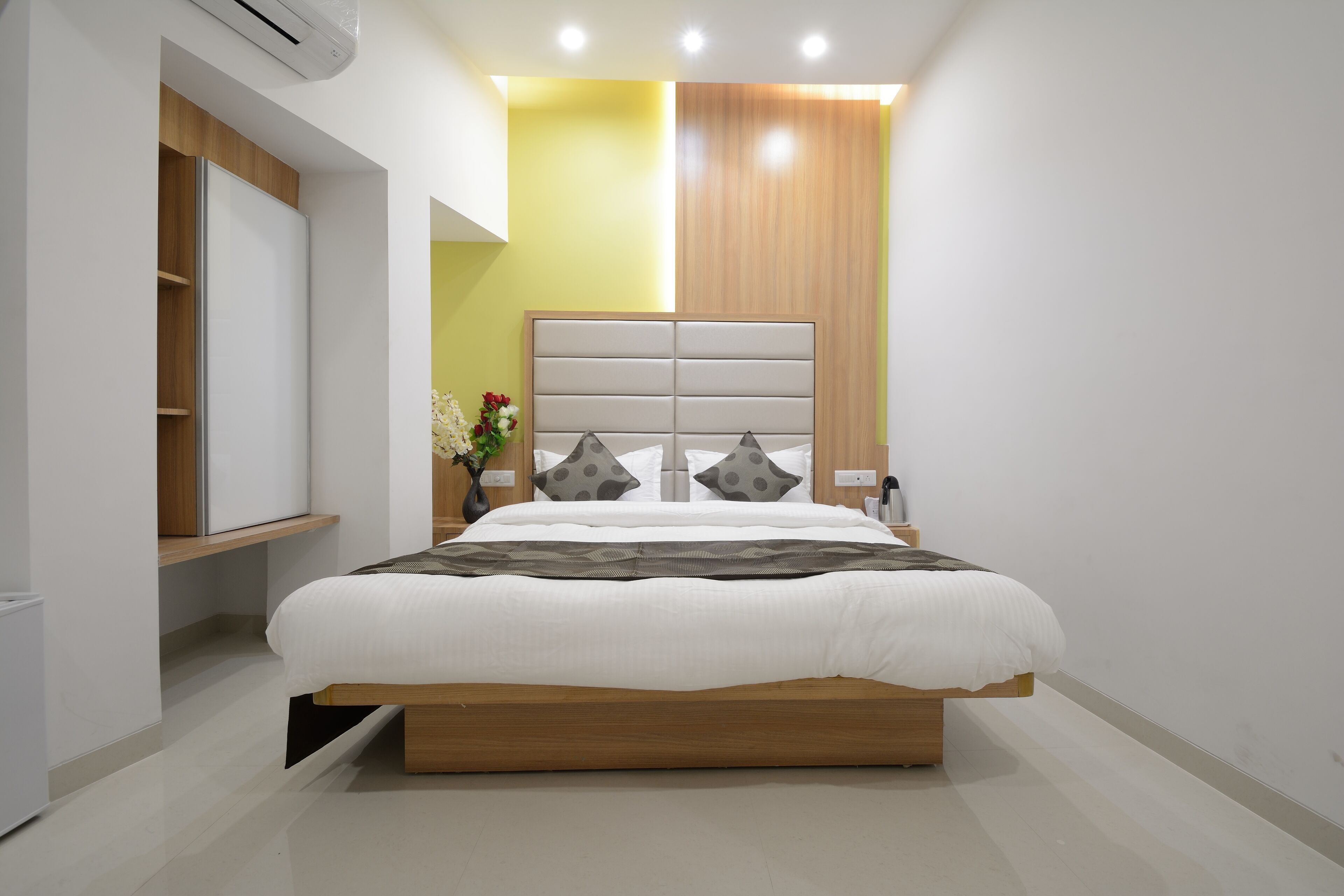 A modern bedroom with a large bed, built-in wardrobe, and a bedside table with a vase of flowers.