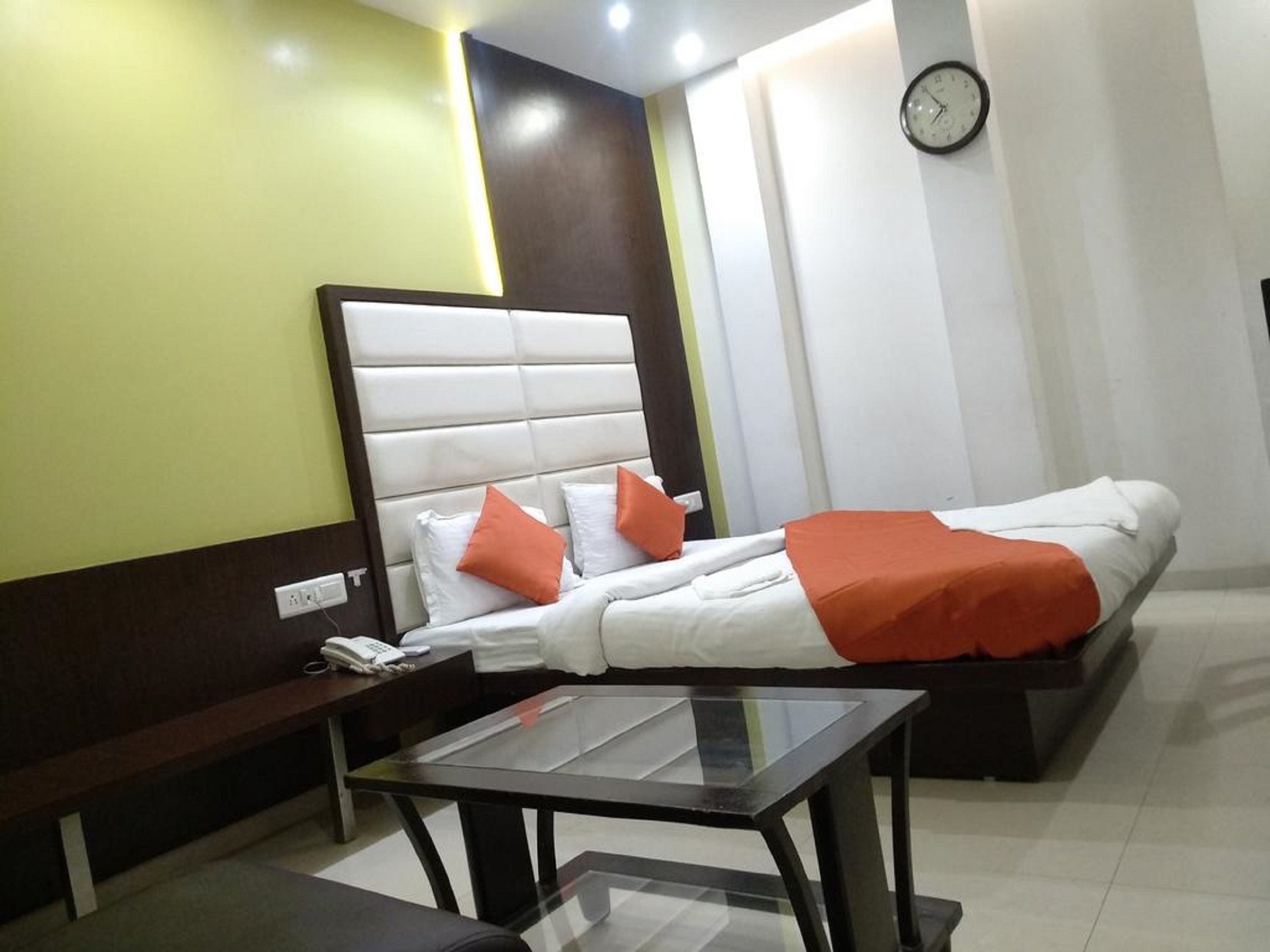 A hotel room with a bed, a bedside table, a telephone, and a clock on the wall.