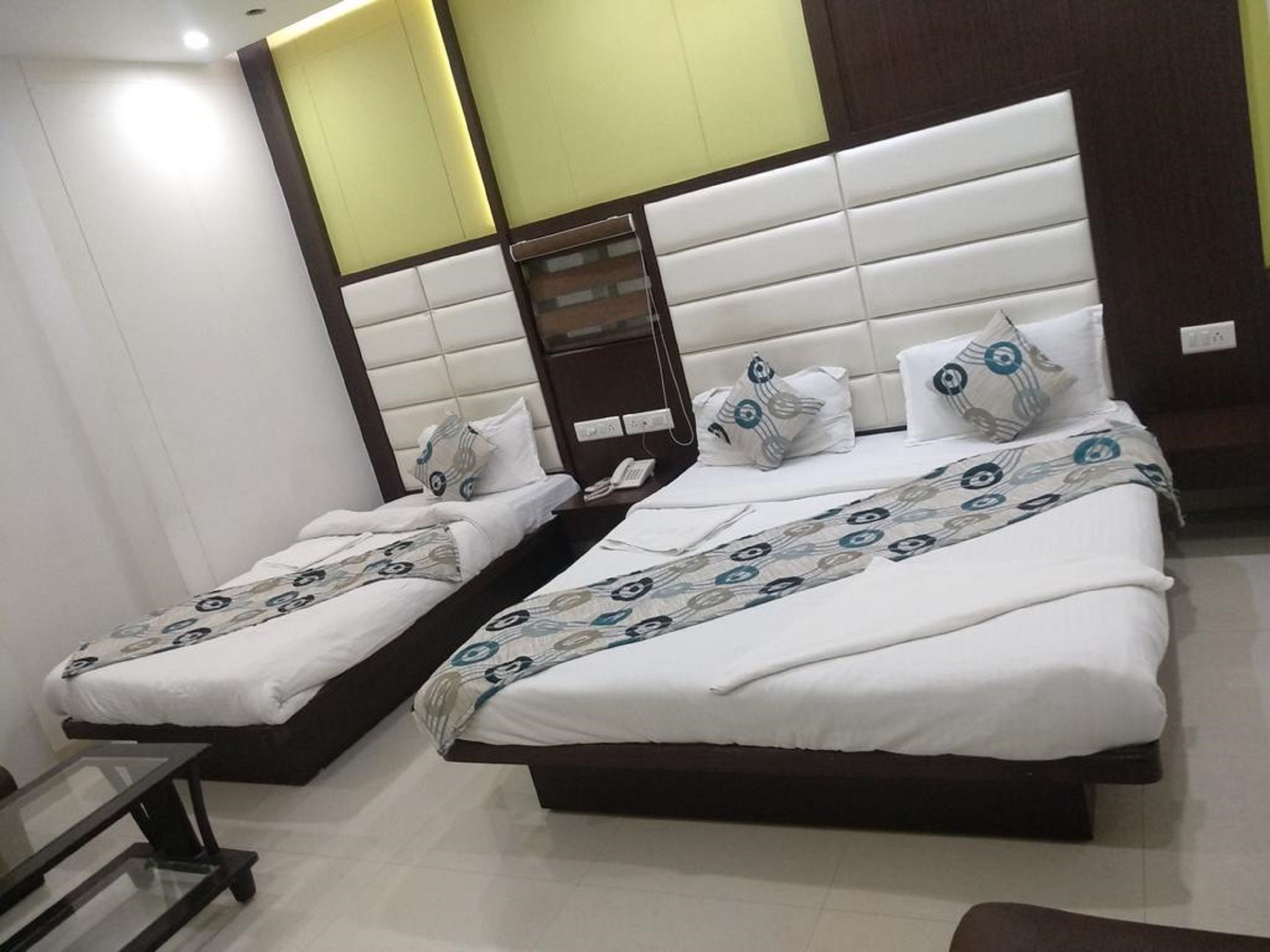 A hotel room with two beds, each with a white bedspread and matching pillows. There is a small table between the beds, and the room has a modern design with a wooden headboard and a light-colored wall.