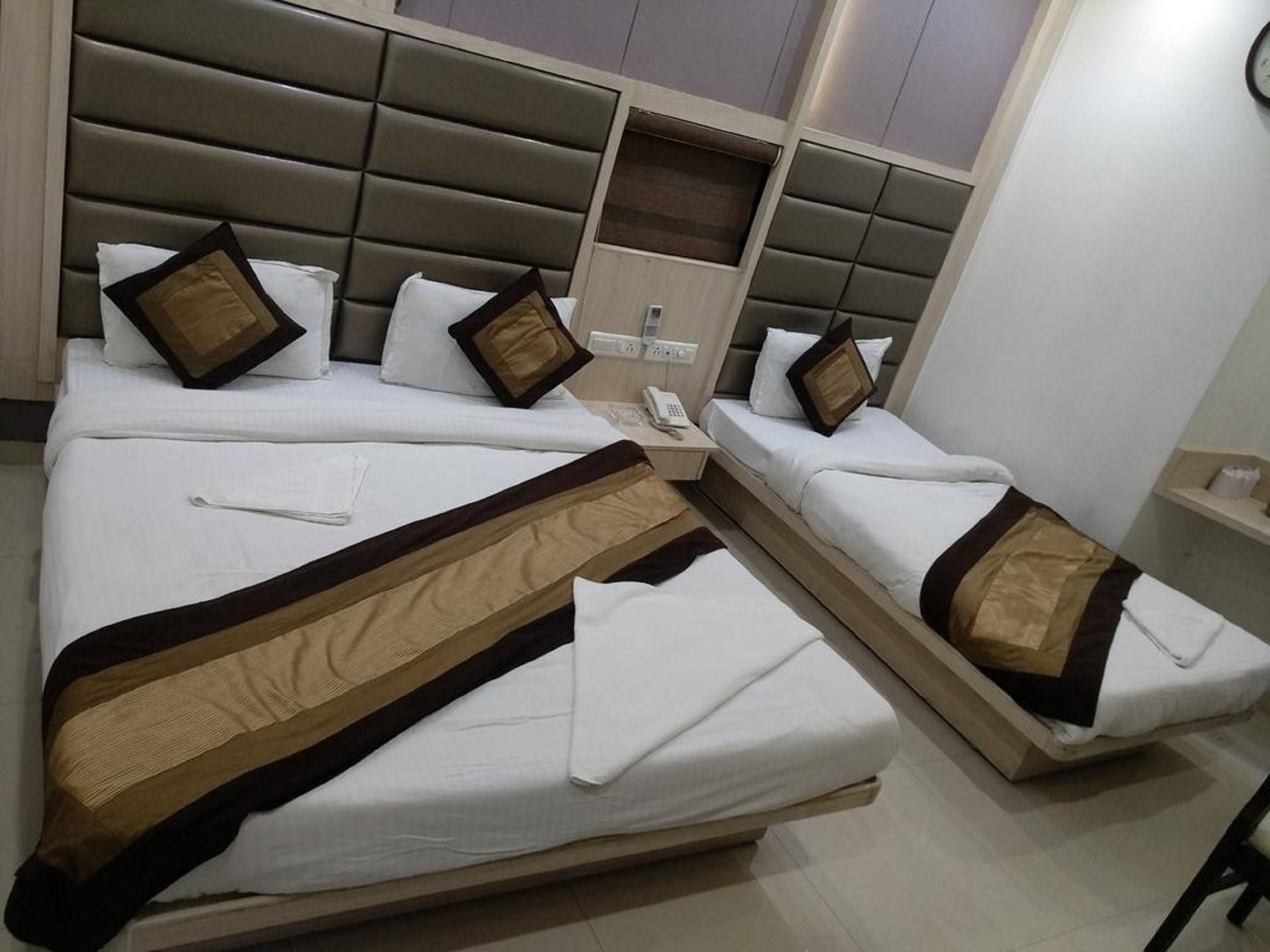 Ein Hotelzimmer mit zwei Betten, jeweils mit weißer Bettwäsche und braunen Akzenten, einem Holzkopfstück, einem Nachttisch mit Telefon und einer kleinen Ablagefläche mit Pflegeprodukten.