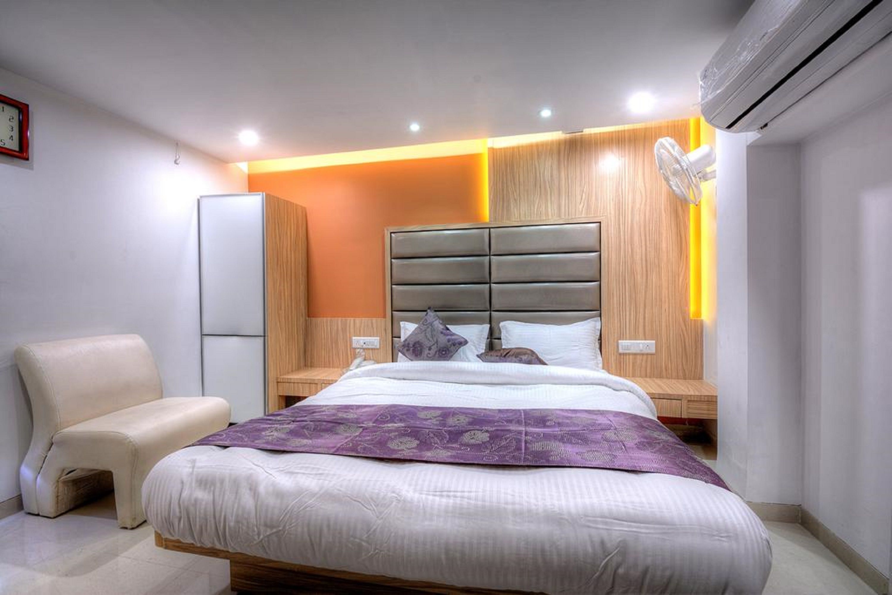 A modern bedroom with a large bed, a bedside table, a chair, and an air conditioning unit.