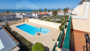 Ein Poolbereich mit freiem Blick auf das Meer, umgeben von Gebäuden mit roten Ziegeldächern und Palmen.