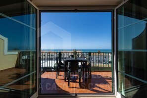 A balcony with a table and chairs, overlooking a beach and the sea.