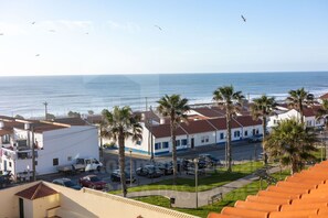A coastal town with a view of the sea, palm trees, and buildings with red roofs.