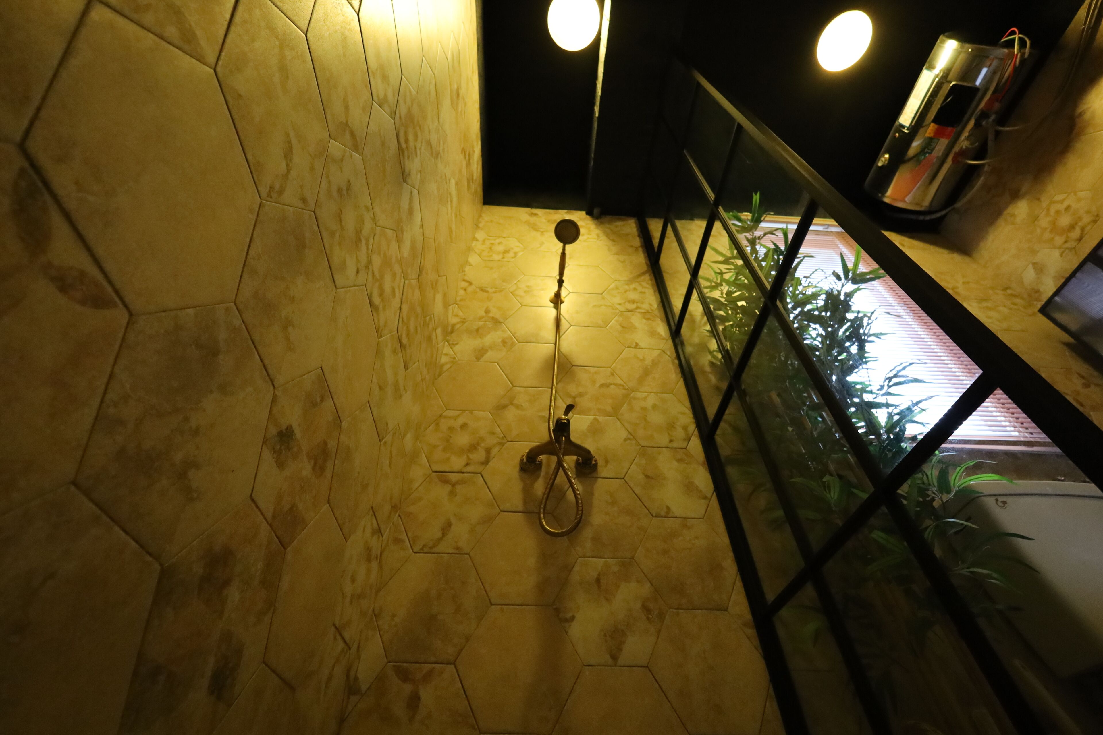 Un baño con baldosas hexagonales, un cabezal de ducha y un secamanos sobre un mostrador.