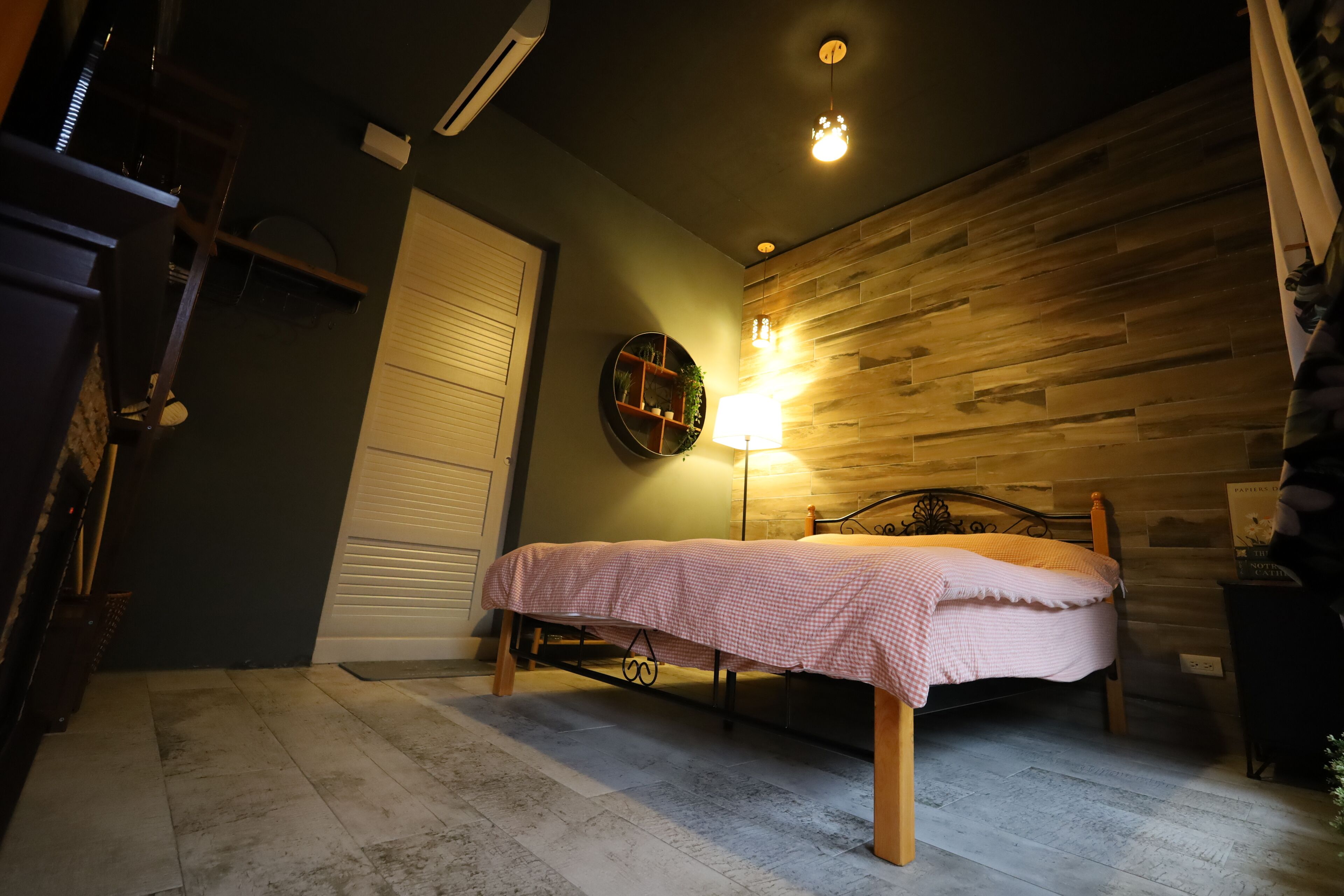 A bedroom with a bed, a wooden wall, a lamp, and a door.