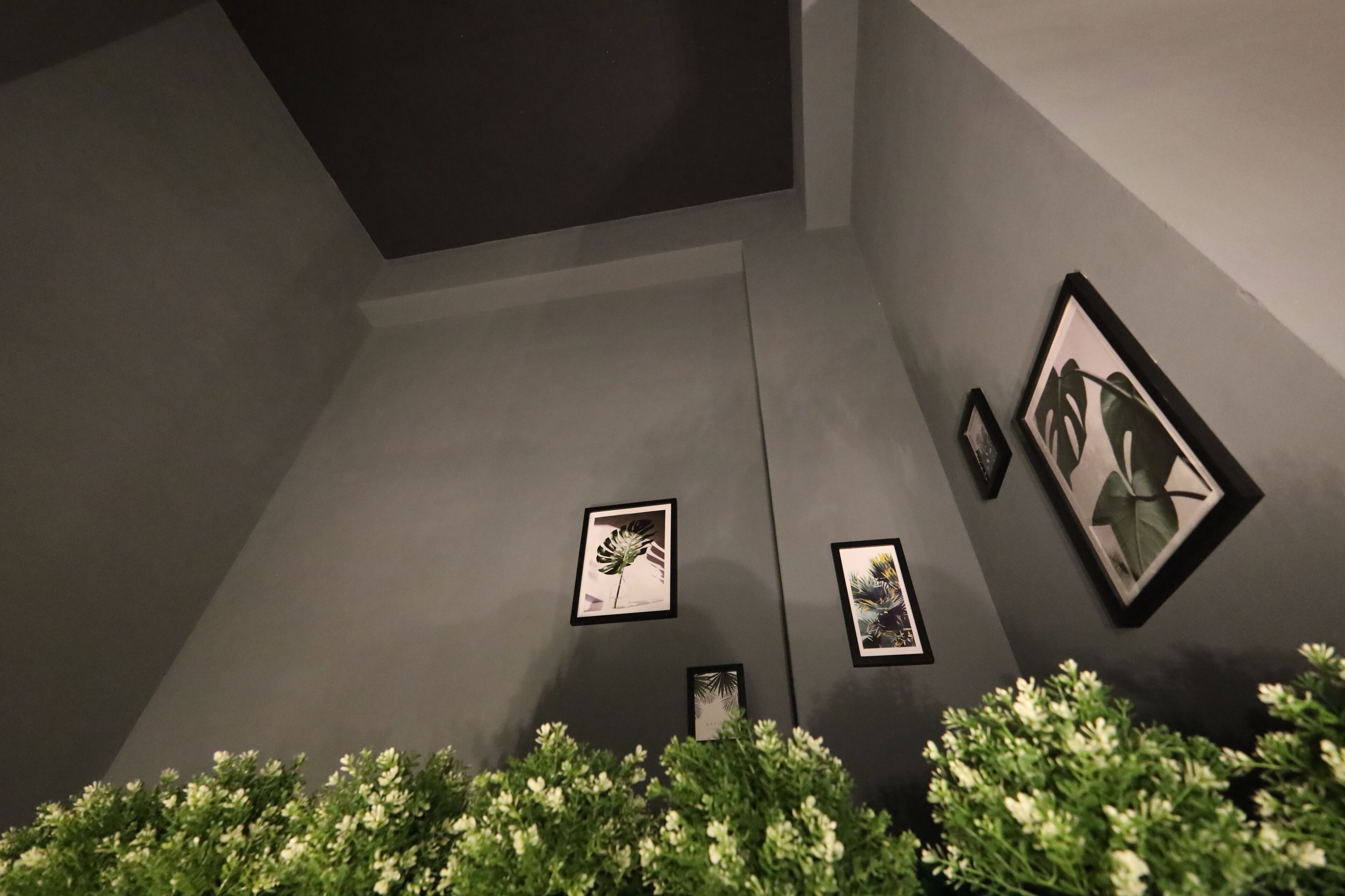 Een kamer met een grijze muur en lijstwerken. Drie schilderijen hangen in de lijst aan de muur.