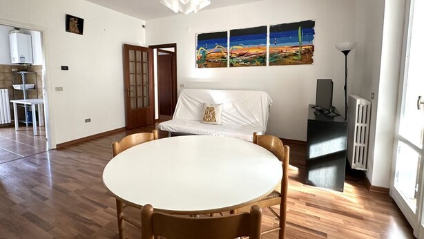 A room with a round dining table, a sofa with a cushion, a painting on the wall, a radiator, and a door. - N194 - Numana, large three-room apartment with garden (Numana)