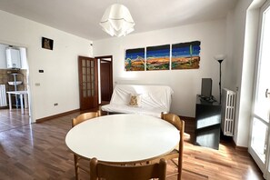 A room with a round dining table, a sofa with a cushion, a painting on the wall, a radiator, and a door. - N194 - Numana, large three-room apartment with garden (Numana)