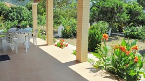 Eine Terrasse im Freien mit Tisch und Stühlen, umgeben von Pflanzen und Blumen.
