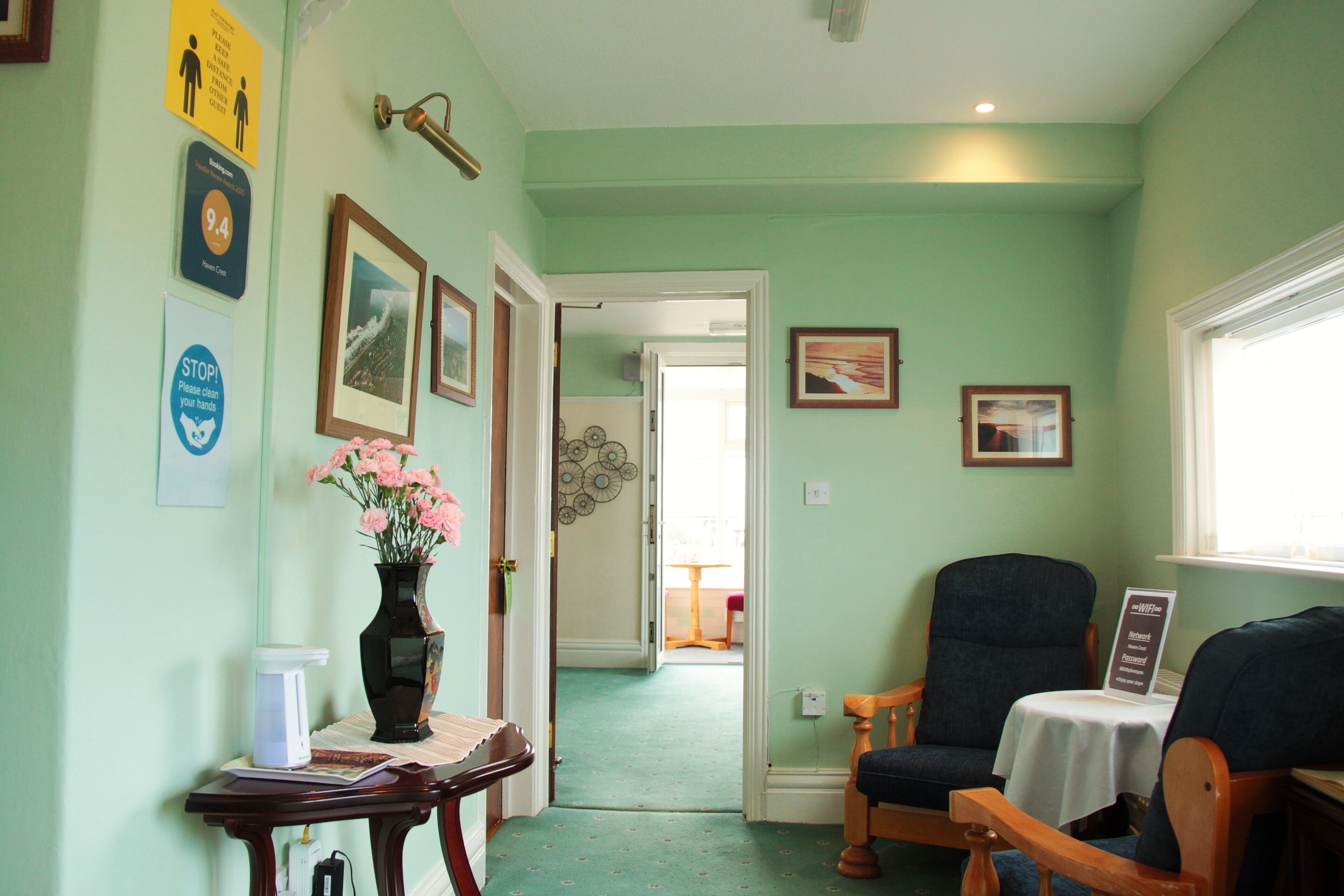 A hallway with a green wall, a wooden table with a vase of flowers, and two chairs.