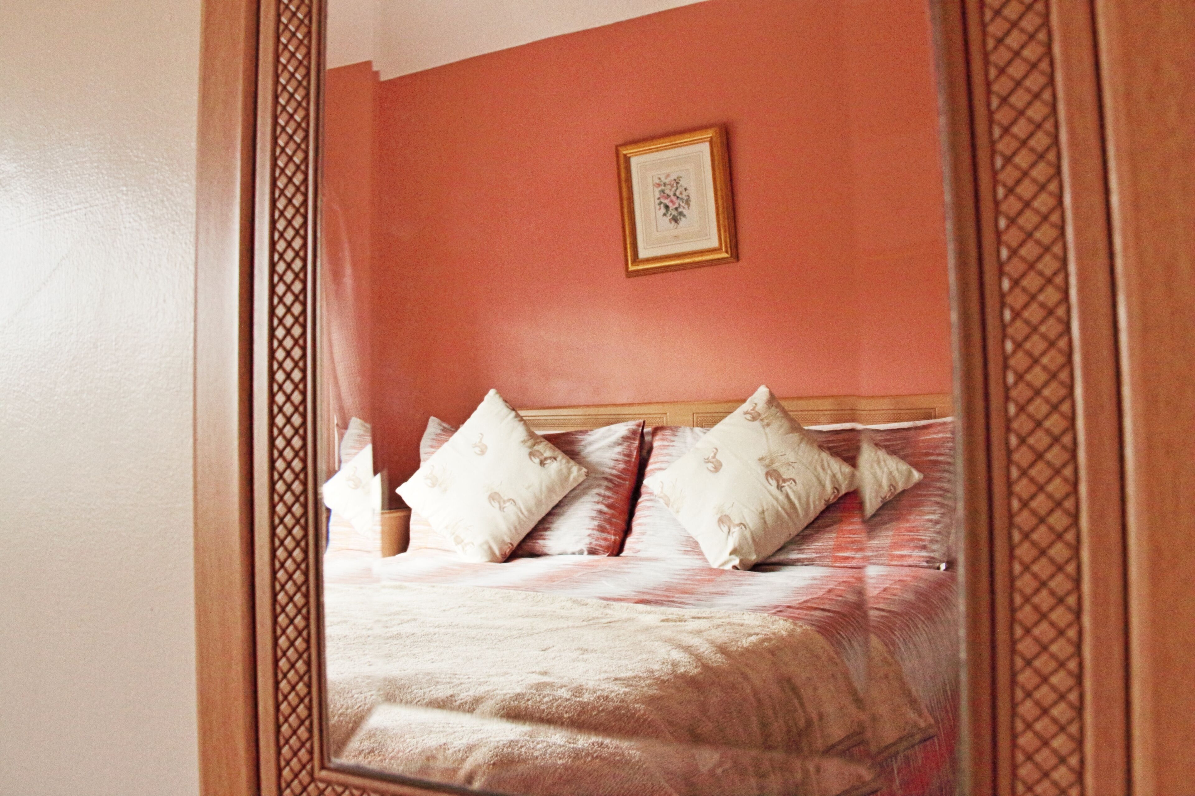 A bedroom with a wooden headboard, a red wall, and a framed picture above the bed.
