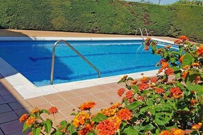 A swimming pool with a metal ladder, surrounded by a tiled deck and vibrant flowers.