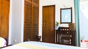 A hotel room with a bed, a wooden wardrobe, a desk with a chair, a potted plant, and a window with curtains. - Atlantic Lodge (Aljezur)