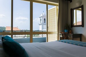 Habitación de hotel con un ventanal grande, una cama, una mesita de noche, una silla y una planta en maceta.
