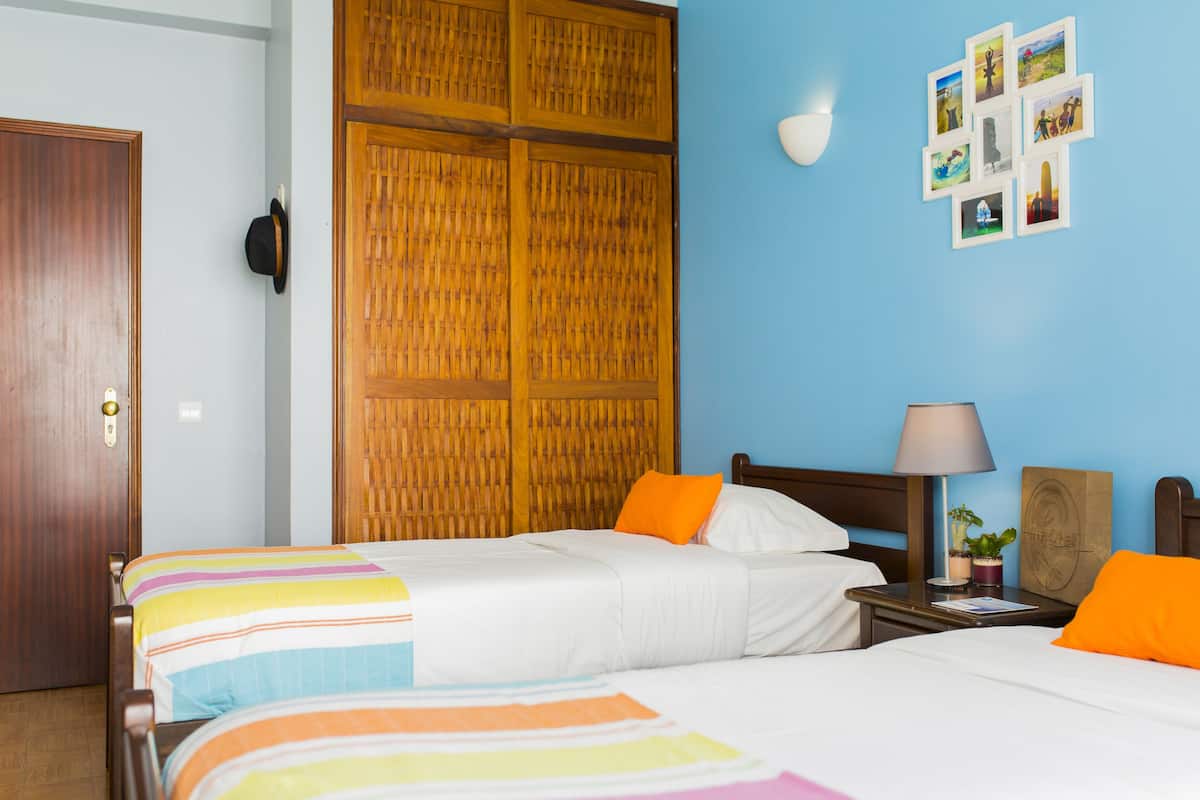 Ein Hotelzimmer mit zwei Betten, einem Holzschrank, einer Wandlampe und einem kleinen Tisch mit einer Pflanze.
