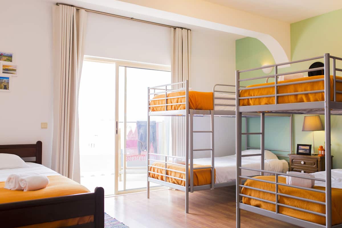 Ein Hotelzimmer mit Etagenbett, einem Einzelbett und einer Schiebetür zu einem Außenbereich.