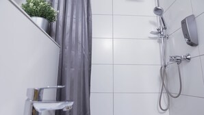 Un baño moderno con un lavamanos blanco, una ducha con cabezal de ducha de mano y una planta en maceta en la pared.