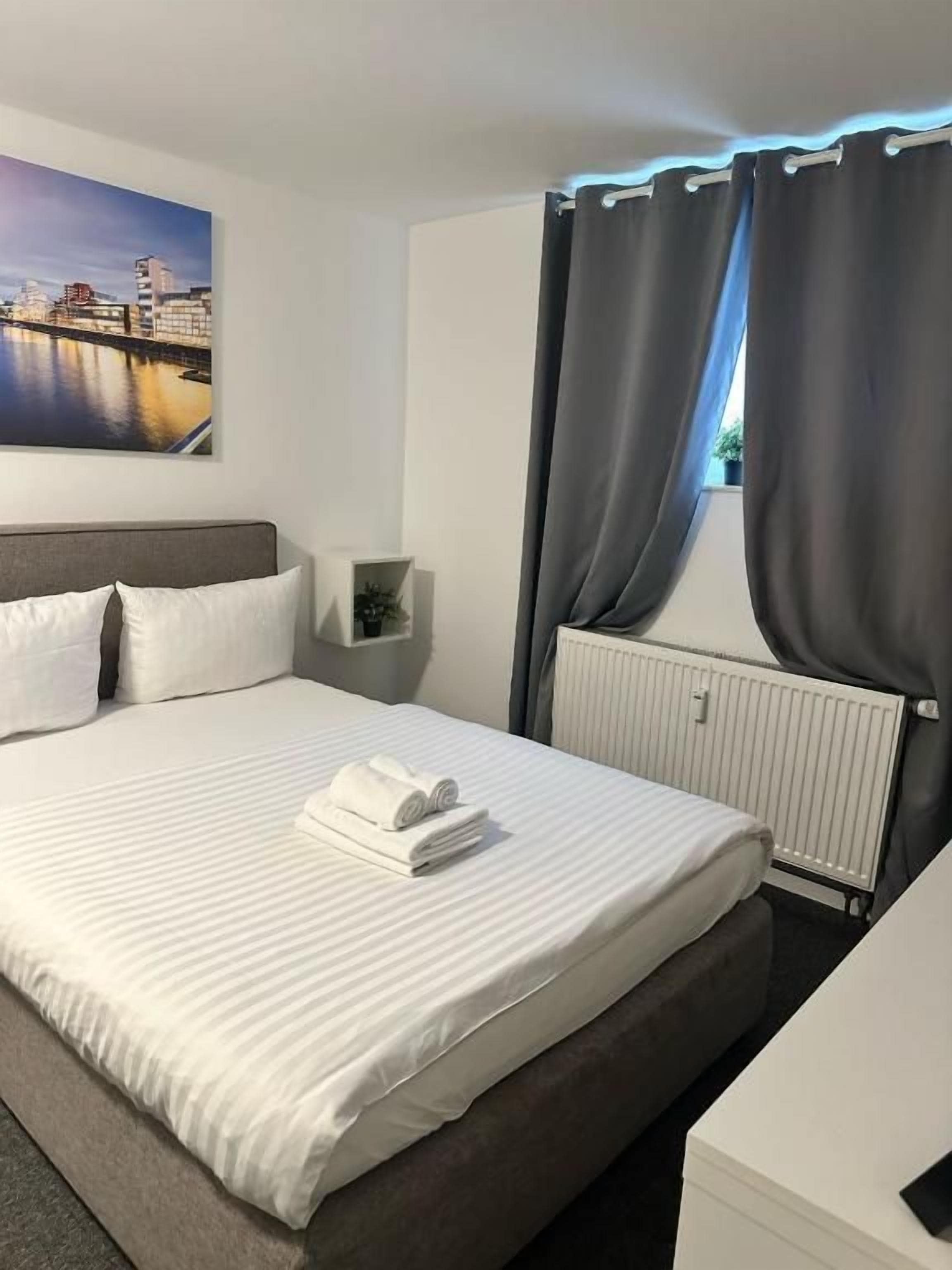 Een hotelkamer met een bed, nachtkastje, raam met gordijnen en uitzicht op de stad.