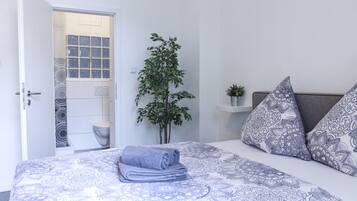 A neatly made bed with patterned bedding, a potted plant, and decorative pillows.