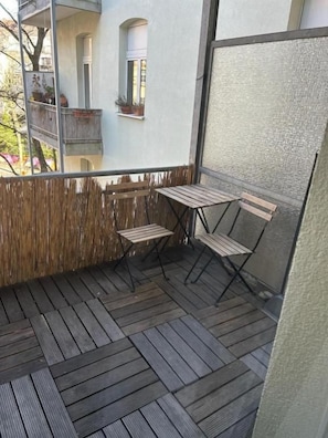 Un balcón con piso de madera, una mesa y dos sillas.