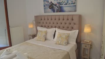 Cama bem arrumada com cabeceira estofada, duas luminárias de apoio e um quadro sobre a cama.