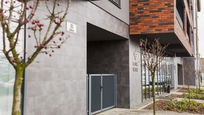 A modern building with a grey facade, a brick section, and a metal gate.