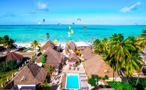 A beach resort with thatched-roof huts, a swimming pool, and a view of the ocean with kite surfers. - Ananda Beach Hotel (Paje)