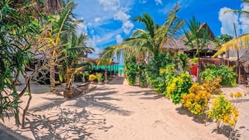 Un resort tropical con cabañas de techo de paja, palmeras y un sendero de arena.