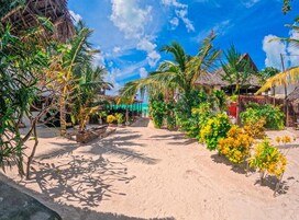 A tropical resort with thatched-roof huts, palm trees, and a sandy pathway.