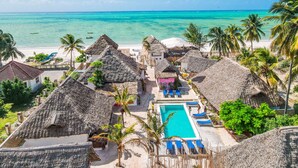 Un complejo turístico en la playa con cabañas de techo de paja, una piscina y vistas al océano.