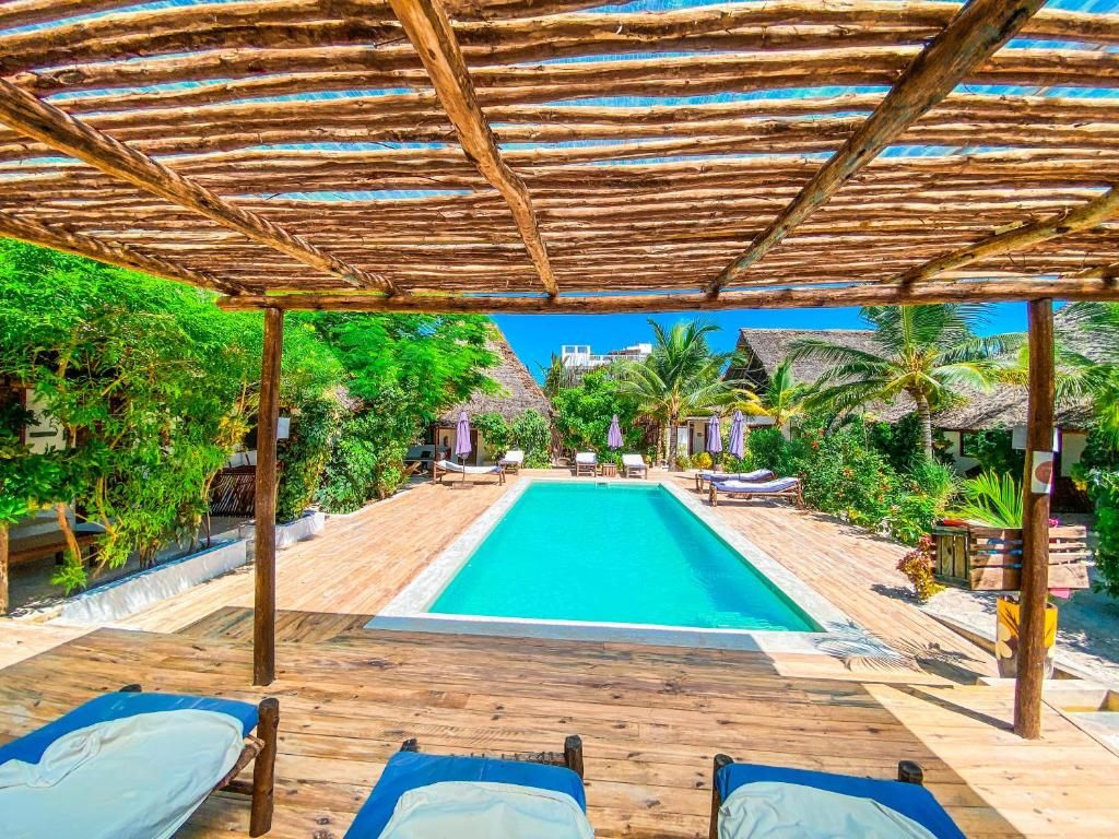 A wooden deck with a pool, lounge chairs, and a thatched roof structure.