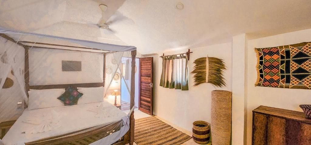 Une pièce avec un lit, une porte en bois, un mur orné d’une tapisserie à motifs et un panier tressé.