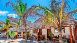 Una propiedad frente a la playa con cabañas de techo de paja, palmeras y una playa arenosa.