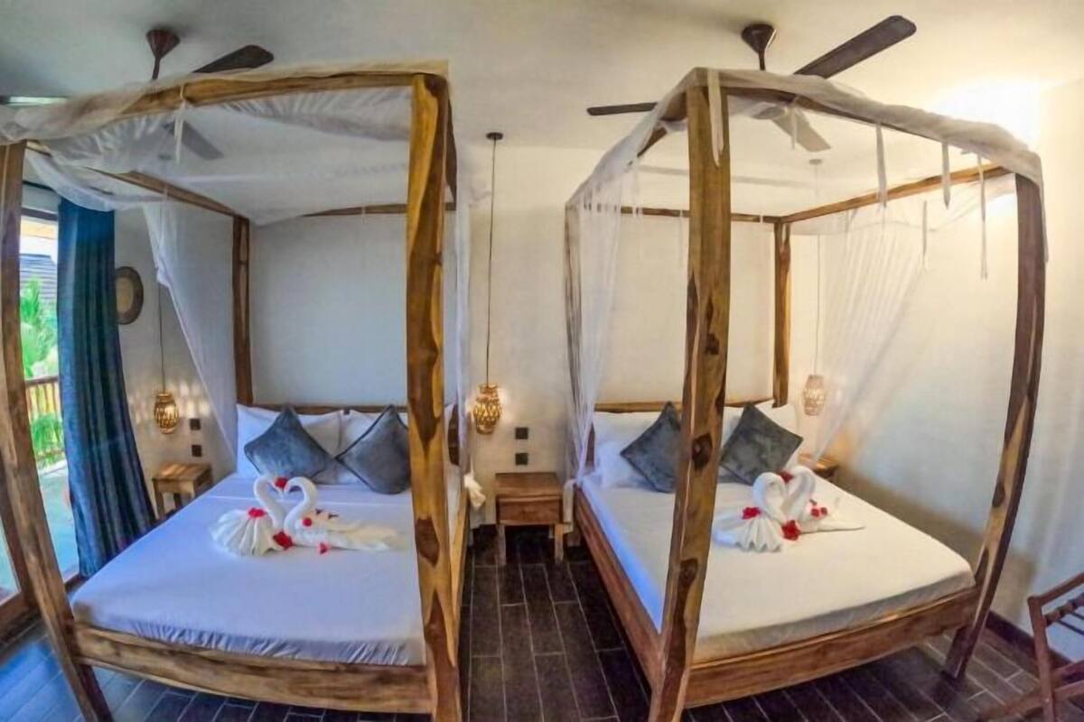 Two wooden four-poster beds with white bedding and swan decorations, a small bedside table, and a ceiling fan.