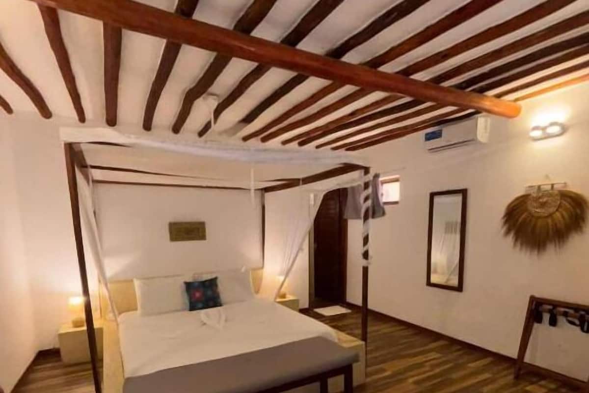 A four-poster bed with a wooden frame, a bedside table, a wall-mounted light, and a framed picture on the wall.