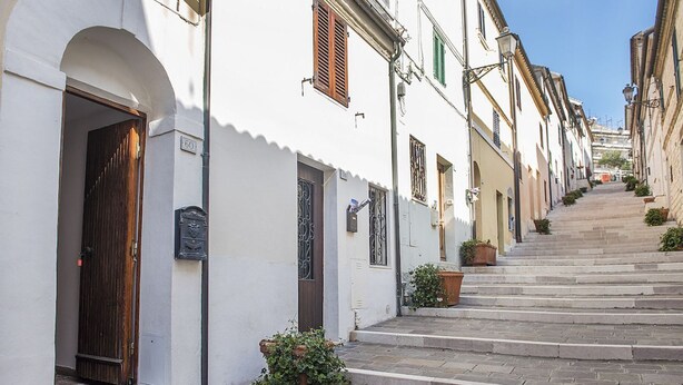 A narrow street with white buildings, a wooden door, and steps leading up to a building.