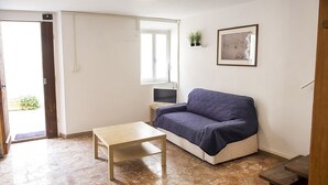 A room with a sofa, a small table, a TV, a window, and a framed picture on the wall.