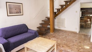 A living room with a sofa, a coffee table, a staircase, and a kitchen visible through an open door.