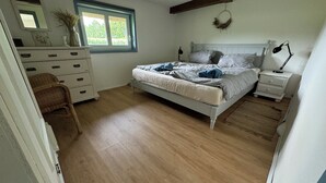 Une chambre à coucher comprenant un lit, une commode, une chaise, une table de chevet, une lampe, une fenêtre et un miroir.