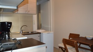 A compact kitchen with a coffee maker, sink, and a small refrigerator. There is a wooden dining table with chairs and a bowl on it. - Best House Petit Pylos Messinias (Pylos-Nestoras)
