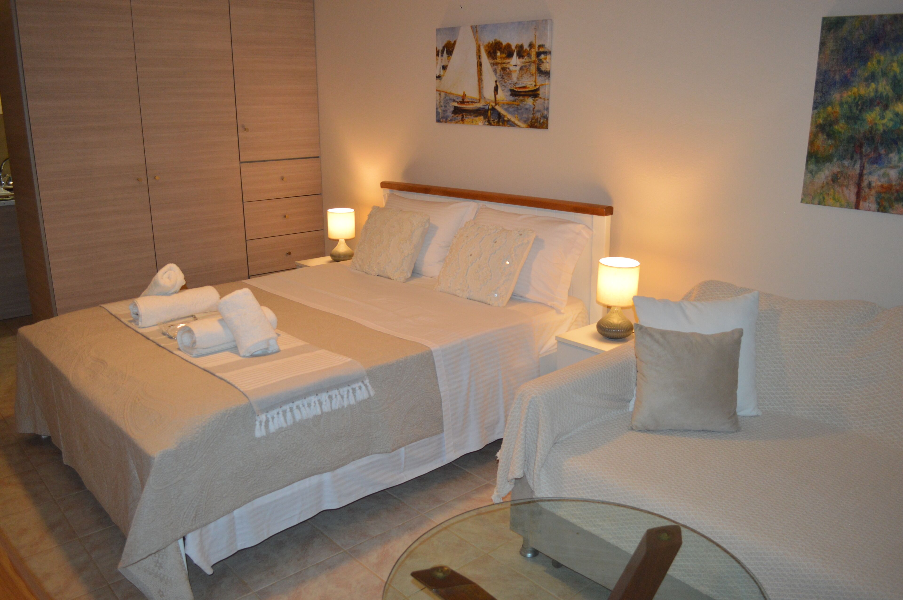 A hotel room with a bed, a sofa, a glass table, and artwork on the walls.